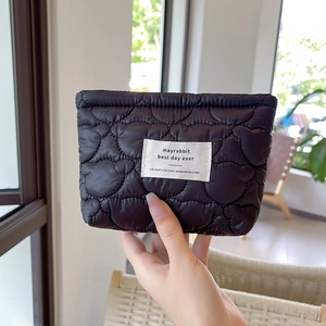 Detailed view of black heart-quilted cosmetic bag with brand label and glossy finish
