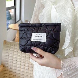 Detail of black quilted cosmetic bag with heart patterns and woven label on front