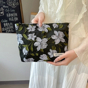Close-up of black cosmetic bag featuring 3D floral embroidery and brand label detail