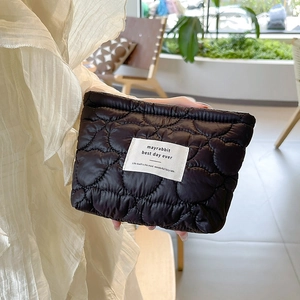 Detail of heart quilted black makeup bag with brand label and fluffy texture