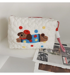 Detail of white quilted cosmetic bag featuring embroidered brown dog and plush colorful dots