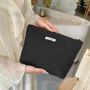 Detail of black quilted cosmetic bag with bear head patterns and woven logo tag