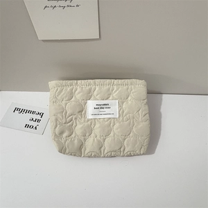 Detail of cream quilted makeup bag featuring bear pattern embroidery and square woven label
