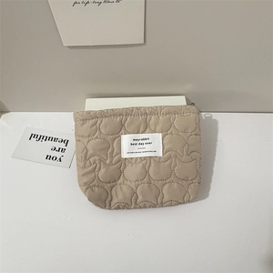Detailed view of beige quilted makeup bag featuring cat head pattern and label