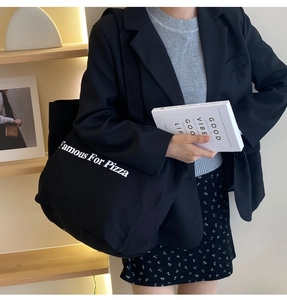 Schwarze Canvas-Tragetasche mit Famous For Pizza Aufdruck über einem schwarzen Blazer