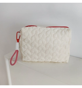 Detail of white heart-quilted pouch featuring red zipper and pink lanyard handle loop