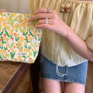 Close-up of hand-held floral makeup bag with yellow tulip pattern and woven logo tag