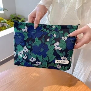Floral jacquard travel cosmetic bag with a zipper and brand label held by a model
