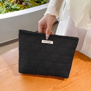 Close-up of black quilted bear pattern cosmetic bag with May Rabbit label on wood