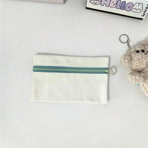 Detail of canvas pouch with dark blue zipper, green ring pull, and plush bear charm