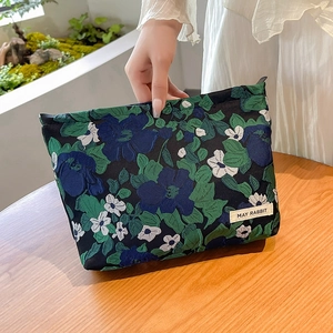 Detail of floral jacquard makeup bag held by hand over a rustic wooden table