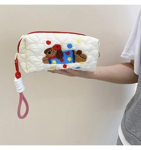 Close-up of white heart-quilted pouch featuring embroidered puppy and red zipper