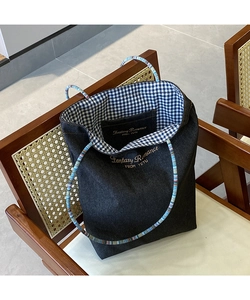 Dettaglio della borsa tote in denim scuro con ricamo e manico intrecciato colorato