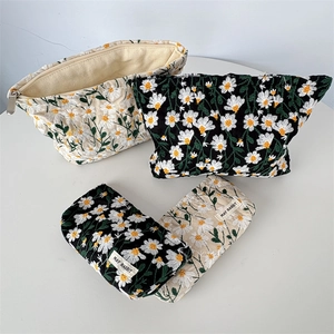Detailed embroidery of white daisies on black and cream canvas cosmetic storage bags