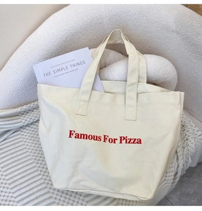 Detail einer beigen Canvas-Tragetasche mit rotem Pizza-Aufdruck auf einem Sessel