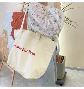 Detailaufnahme der großen weißen Canvas-Tragetasche mit Famous For Pizza-Aufdruck am Model