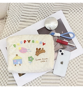 Detail of cream quilted makeup bag featuring colorful puppy embroidery and blue knot charm