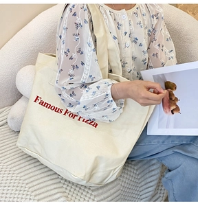 Detail der geräumigen cremefarbenen Canvas-Tasche mit Famous For Pizza Slogan beim Tragen