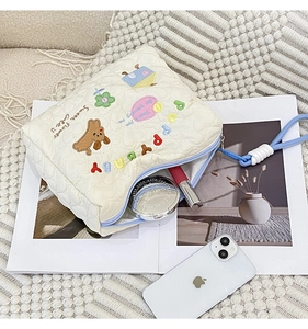 Detail of white quilted cosmetic bag with puppy embroidery and portable lanyard handle