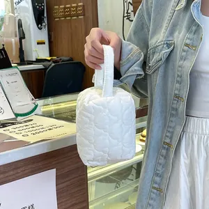 Vue détaillée d'une trousse de maquillage blanche matelassée tenue par la main