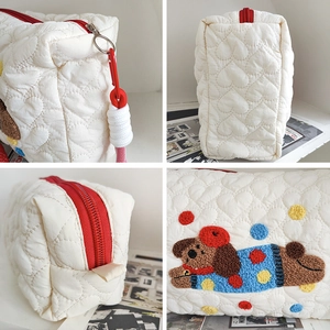 Detail view of heart-quilted white bag with dog embroidery and red zipper hook