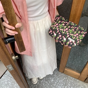 Chic floral makeup bag with pink tulips and brand label held by a model in outdoor setting