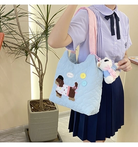Detailed close-up of quilted light blue shoulder bag with cute puppy embroidery and bear charm