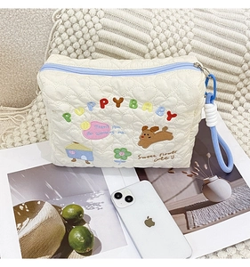 Detail of white quilted makeup bag featuring colorful puppy embroidery and blue zipper