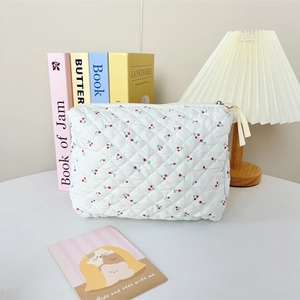 Detailed texture of white quilted makeup bag with red cherry print and ribbon zipper pull