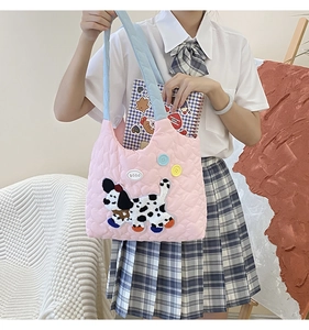 Detail of pink quilted shoulder bag featuring cute puppy patch and wide blue strap