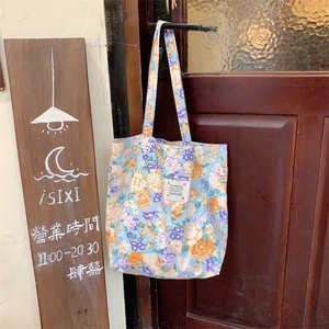 Gros plan sur un cabas floral bleu vintage suspendu à une poignée de porte en bois