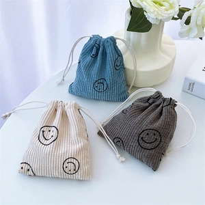 Close-up of corduroy drawstring pouches in cream, blue and grey with embroidered smile face