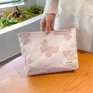 Pink jacquard makeup bag with 3D bow patterns and May Rabbit label on a wooden table