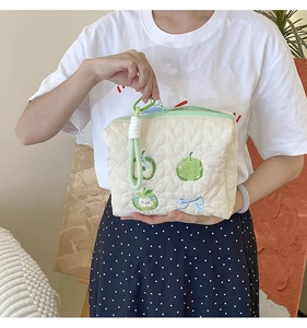 Quilted white cosmetic bag with apple embroidery and green woven wristlet strap detail