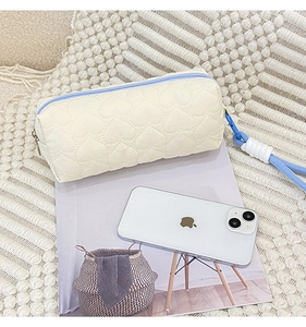 Close-up of quilted cream makeup bag with heart pattern and blue woven lanyard