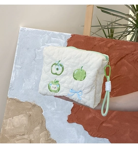 Close-up of white quilted cosmetic bag with green apple and blue bow embroidery detail
