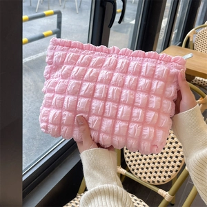 Pink bubble cloud makeup bag with ruffled edge shown in a hand-held outdoor setting