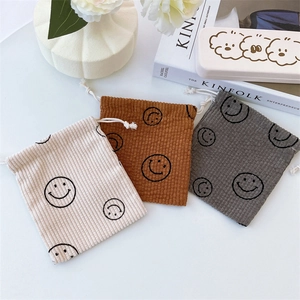 Macro shot of three corduroy drawstring bags in cream, brown and grey with smiley faces