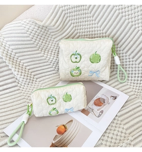 Detail of cream quilted cotton bags with apple embroidery and green handle strap