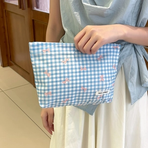 Dettaglio della borsa cosmetica a quadri blu con fiocchi rosa tenuta in mano