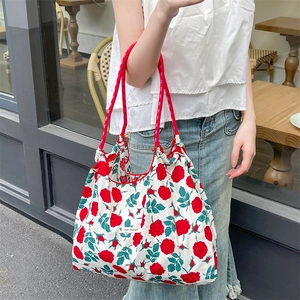 Borsa tote in tela floreale con rose rosse e manici in corda in un ambiente da caffè