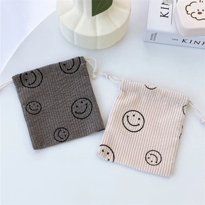 Detail of corduroy drawstring pouches in grey and beige with minimalist smiley face logo