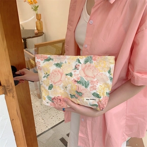 Detail shot of floral makeup bag with pink roses and woven label held by a model