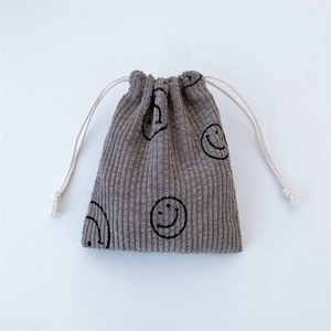 Detailed texture of gray corduroy drawstring bag featuring a black smiley face print