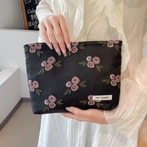 Detailed embroidery of pink roses on a premium black satin makeup bag held by a model