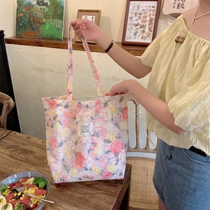 Détail du sac cabas en toile fleurie avec écusson lapin posé sur une table en bois
