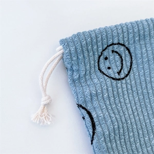 Detail of blue corduroy storage bag showing textured fabric and black smiley embroidery