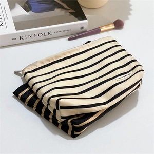 Striped satin toiletry bag with zipper closure and logo patch on white desk