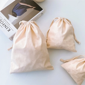 Three sizes of beige cotton drawstring canvas bags with clear texture on a desk