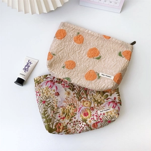 Detailed view of embossed floral and citrus patterned makeup bags with woven brand label